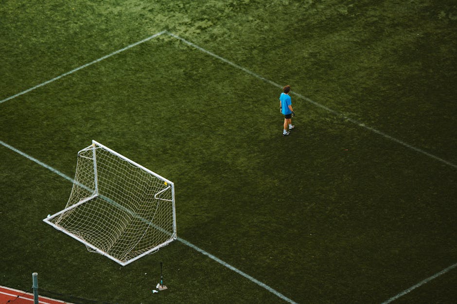Aerial view of a lone soccer player engaged in individual soccer training near a goal on a grassy field.