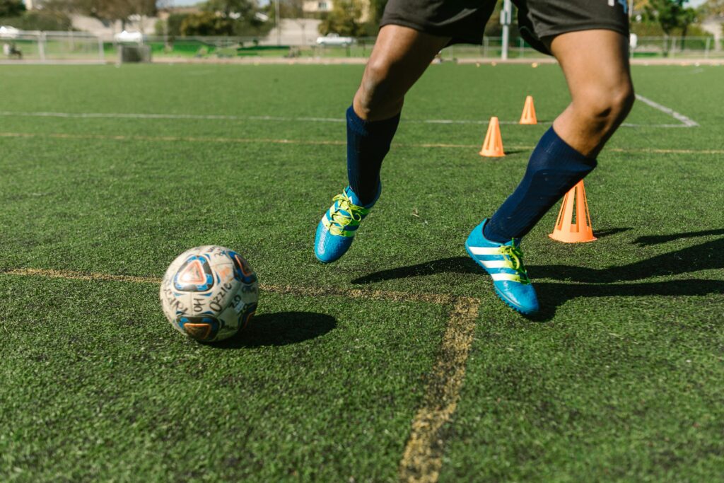 Soccer player practicing solo soccer drills on a grass field with vibrant shoes and cones.